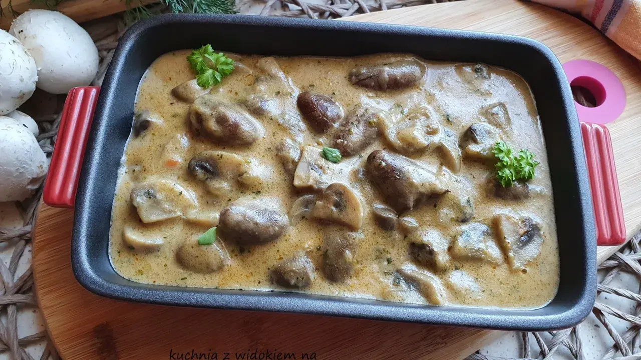 Gulasz z serc drobiowych w kremowym sosie, udekorowany natką pietruszki. Obok leżą świeże pieczarki i gałązki koperku.