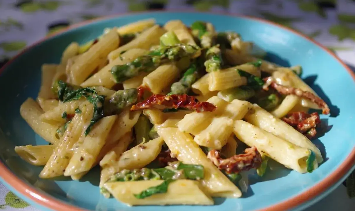 Penne z kremowym sosem, zielonymi szparagami i suszonymi pomidorami. Pyszny makaron ze szparagami na talerzu.
