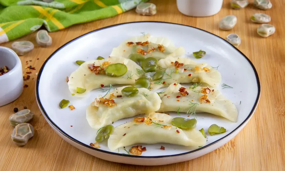 Pyszne pierogi z bobem, posypane skwarkami i koperkiem, prezentują się apetycznie na talerzu.