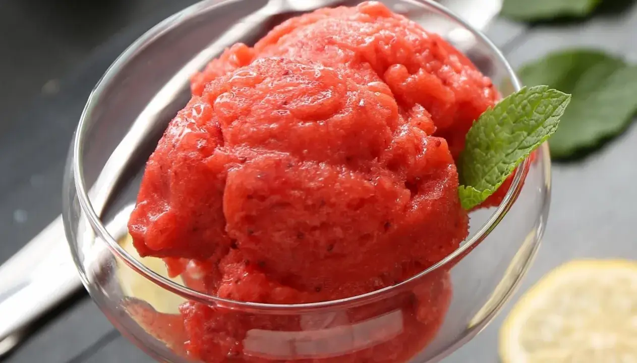 Orzeźwiający sorbet z arbuza w szklanej miseczce, ozdobiony listkiem mięty i plasterkiem cytryny. Idealny na upalne dni.