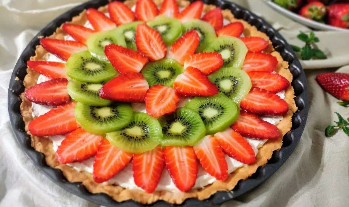 Kolorowa tarta z owocami: plasterki kiwi i truskawek ułożone na kremowym nadzieniu.
