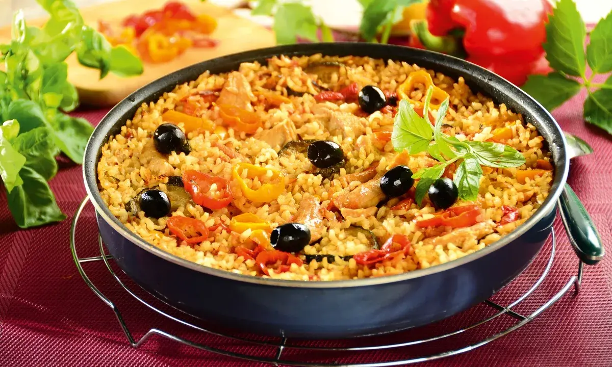 Pyszna paella z kurczakiem, ryżem, papryką, oliwkami i ziołami, podana w głębokiej patelni.