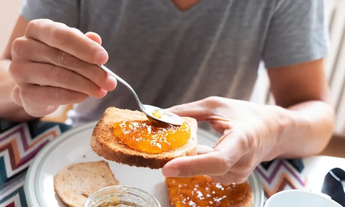 Osoba smaruje łyżeczką tost pysznym dżemem z nektarynek. Słodki początek dnia.