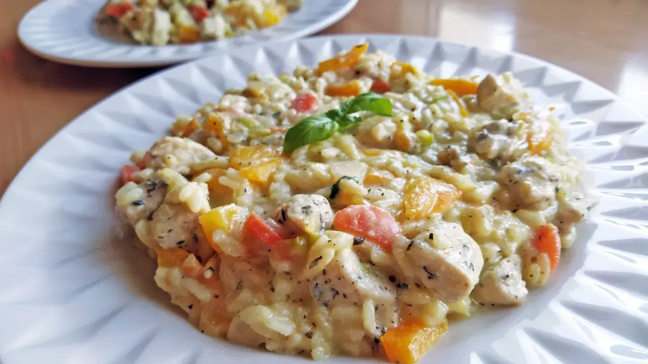 Pyszne, klasyczne risotto z kurczakiem i kolorowymi warzywami, udekorowane listkiem bazylii. Idealne na obiad.