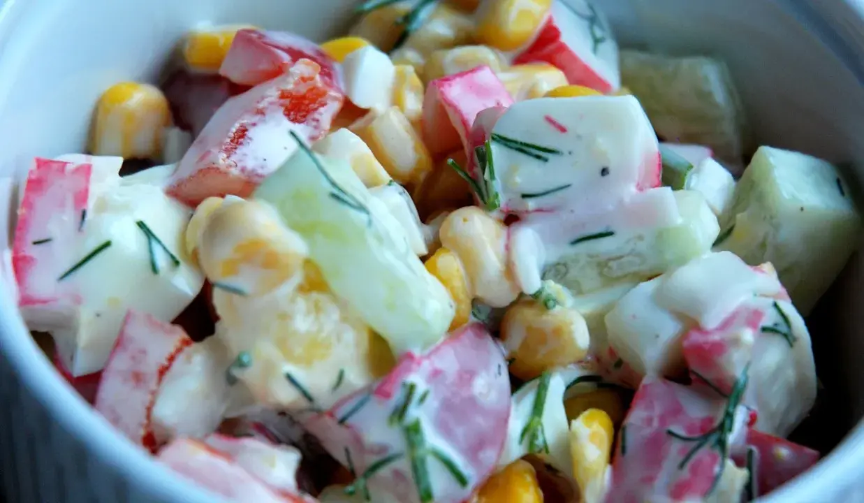 Pyszna sałatka z surimi, kukurydzy, ogórka i papryki, polana kremowym sosem i posypana koperkiem.