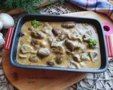 Gulasz z serc drobiowych w kremowym sosie, udekorowany natką pietruszki. Obok leżą świeże pieczarki i gałązki koperku.