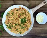 Penne z kremowym sosem i kawałkami pikantnego chorizo, posypane świeżą natką pietruszki. Obok miseczka z parmezanem.