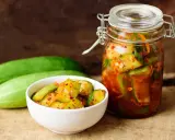 Pikantne ogórki z papryką chili w słoiku i miseczce, obok świeże ogórki.