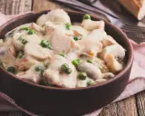 Pyszny strogonow z kurczaka z pieczarkami i groszkiem w kremowym sosie, podany w glinianej misce na drewnianym stole.