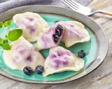 Pyszne pierogi z jagodami na turkusowym talerzu, ozdobione świeżymi borówkami i gałązką ziół.