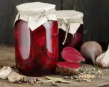 Słoiki z buraczkami w zalewie octowej, obok świeże buraki, czosnek i przyprawy. Domowe przetwory gotowe na zimę.