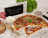 Domowa pizza bez drożdży, z kiełbasą i warzywami, prezentowana na białym papierze, obok sosu i przypraw.