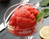 Orzeźwiający sorbet z arbuza w szklanej miseczce, ozdobiony listkiem mięty i plasterkiem cytryny. Idealny na upalne dni.