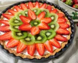 Kolorowa tarta z owocami: plasterki kiwi i truskawek ułożone na kremowym nadzieniu.