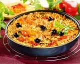 Pyszna paella z kurczakiem, ryżem, papryką, oliwkami i ziołami, podana w głębokiej patelni.