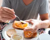 Osoba smaruje łyżeczką tost pysznym dżemem z nektarynek. Słodki początek dnia.