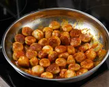 Kiełbasa z cebulą duszona na patelni w sosie. Aromatyczne kawałki mięsa w bogatym, pomarańczowym sosie.