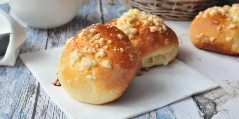 Pyszne drożdżówki z serem, posypane kruszonką, czekają na śniadanie. Obok biała filiżanka z mlekiem.