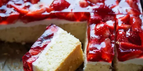 Pyszny biszkopt z galaretką i kremem budyniowym, ozdobiony świeżymi truskawkami. Idealny deser na letnie popołudnie.