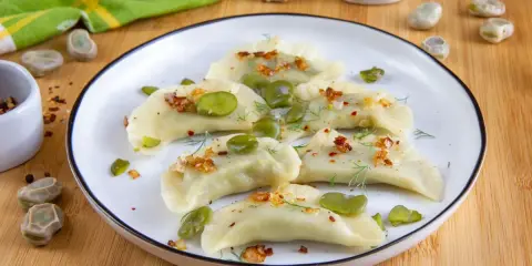 Pyszne pierogi z bobem, posypane skwarkami i koperkiem, prezentują się apetycznie na talerzu.