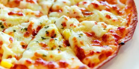 Pyszna pizza z tortilli, obficie posypana serem i ziołami, pokrojona na trójkątne kawałki.