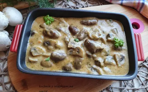 Gulasz z serc drobiowych w kremowym sosie, udekorowany natką pietruszki. Obok leżą świeże pieczarki i gałązki koperku.