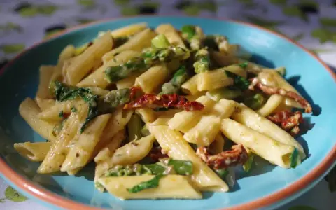 Penne z kremowym sosem, zielonymi szparagami i suszonymi pomidorami. Pyszny makaron ze szparagami na talerzu.