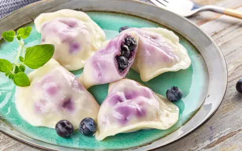 Pyszne pierogi z jagodami na turkusowym talerzu, ozdobione świeżymi borówkami i gałązką ziół.