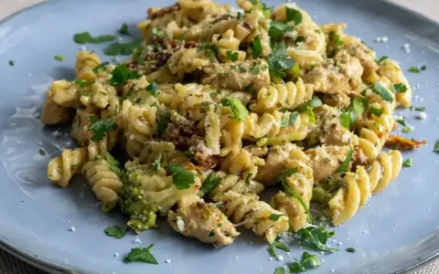 Pyszny makaron z brokułami, kurczakiem i suszonymi pomidorami, posypany parmezanem i natką pietruszki.