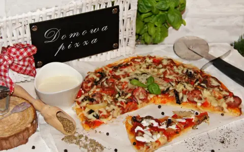 Domowa pizza bez drożdży, z kiełbasą i warzywami, prezentowana na białym papierze, obok sosu i przypraw.