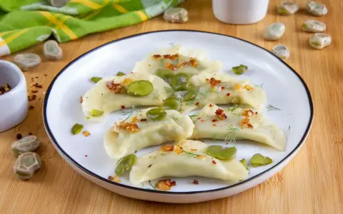 Pyszne pierogi z bobem, posypane skwarkami i koperkiem, prezentują się apetycznie na talerzu.