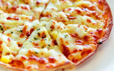 Pyszna pizza z tortilli, obficie posypana serem i ziołami, pokrojona na trójkątne kawałki.