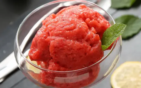 Orzeźwiający sorbet z arbuza w szklanej miseczce, ozdobiony listkiem mięty i plasterkiem cytryny. Idealny na upalne dni.