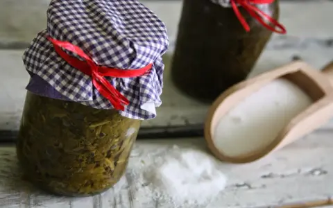 Słoiki z przetworzonym szczawiem na zimę, obok drewniana łopatka z solą.