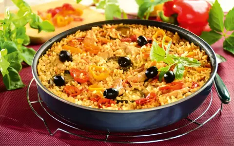 Pyszna paella z kurczakiem, ryżem, papryką, oliwkami i ziołami, podana w głębokiej patelni.