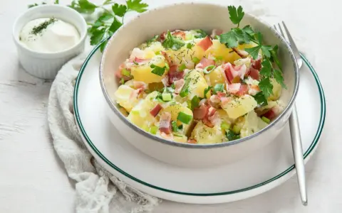 Pyszna sałatka ziemniaczana z boczkiem, posypana szczypiorkiem i natką pietruszki, podana z majonezem.