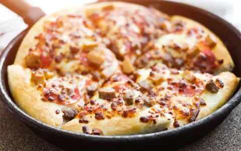 Pyszna pizza z patelni, z ciągnącym się serem i kawałkami mięsa, gotowa do podania.