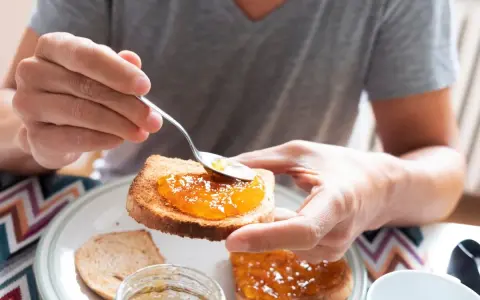 Osoba smaruje łyżeczką tost pysznym dżemem z nektarynek. Słodki początek dnia.