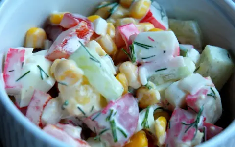 Pyszna sałatka z surimi, kukurydzy, ogórka i papryki, polana kremowym sosem i posypana koperkiem.