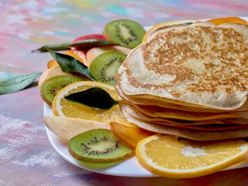 Stos puszystych naleśników z budyniem, udekorowany plasterkami kiwi, pomarańczy i jabłka.