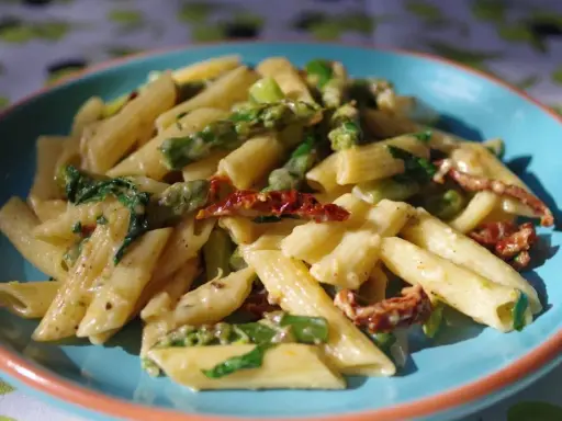 Penne z kremowym sosem, zielonymi szparagami i suszonymi pomidorami. Pyszny makaron ze szparagami na talerzu.