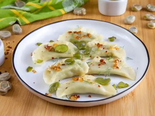 Pyszne pierogi z bobem, posypane skwarkami i koperkiem, prezentują się apetycznie na talerzu.