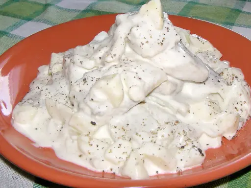 Pyszne śledzie w śmietanie, doprawione pieprzem, podane na pomarańczowym talerzu.