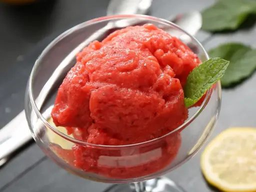 Orzeźwiający sorbet z arbuza w szklanej miseczce, ozdobiony listkiem mięty i plasterkiem cytryny. Idealny na upalne dni.