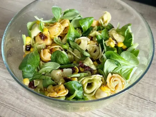 Kolorowa sałatka z tortellini, kukurydzą i suszonymi pomidorami w szklanej misce. Idealna na lekki posiłek.