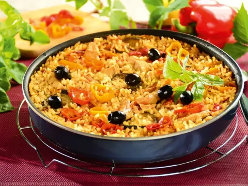 Pyszna paella z kurczakiem, ryżem, papryką, oliwkami i ziołami, podana w głębokiej patelni.