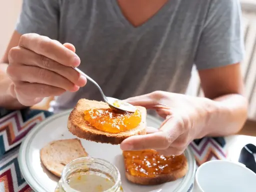 Osoba smaruje łyżeczką tost pysznym dżemem z nektarynek. Słodki początek dnia.