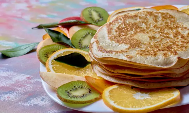 Stos puszystych naleśników z budyniem, udekorowany plasterkami kiwi, pomarańczy i jabłka.