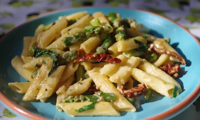 Penne z kremowym sosem, zielonymi szparagami i suszonymi pomidorami. Pyszny makaron ze szparagami na talerzu.