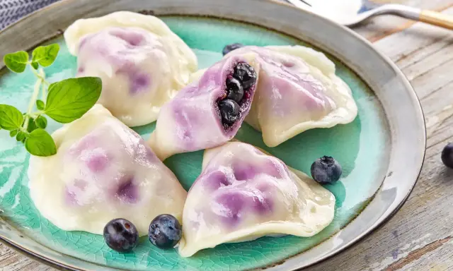 Pyszne pierogi z jagodami na turkusowym talerzu, ozdobione świeżymi borówkami i gałązką ziół.